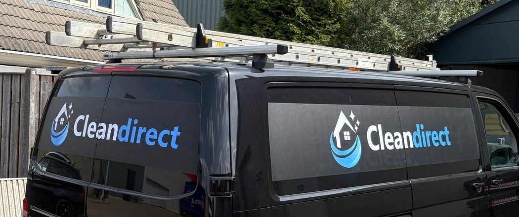De zwarte bus van CleanDirect met het logo op de zij- en achterramen en ladders op het dak
